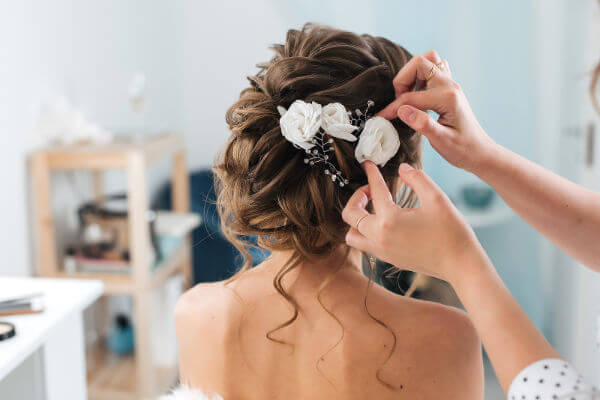 Hair stylist makes an elegant updo styling bride with white flowers in her hair
