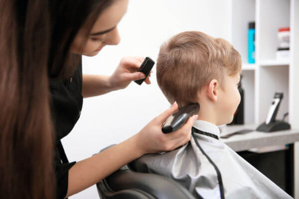 Little boy getting clipper haircut from professional hair stylist at salon