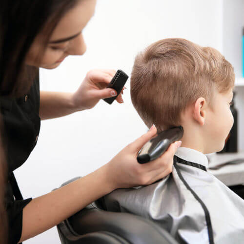 Professional hair stylist giving a haircut to a little boy in salon