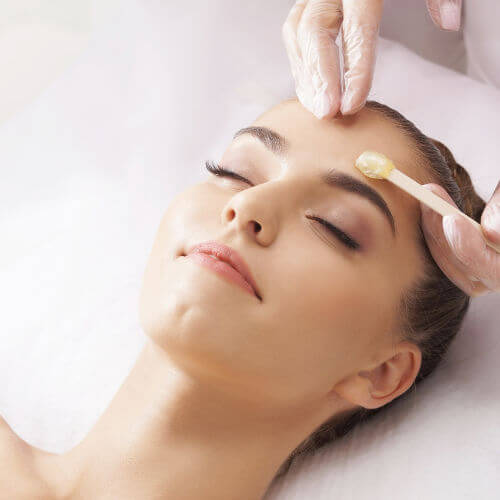 Professional salon worker applying wax and removing hair via eyebrow wax salon treatment