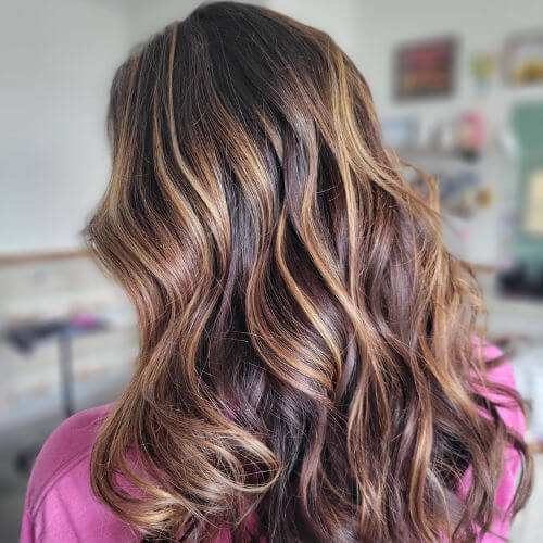 Back view of long brunette hair with glossy caramel balayage and soft waves for a professionally styled look