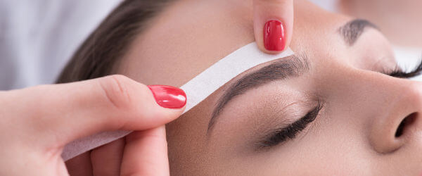 Pretty woman getting eyebrow waxing in salon
